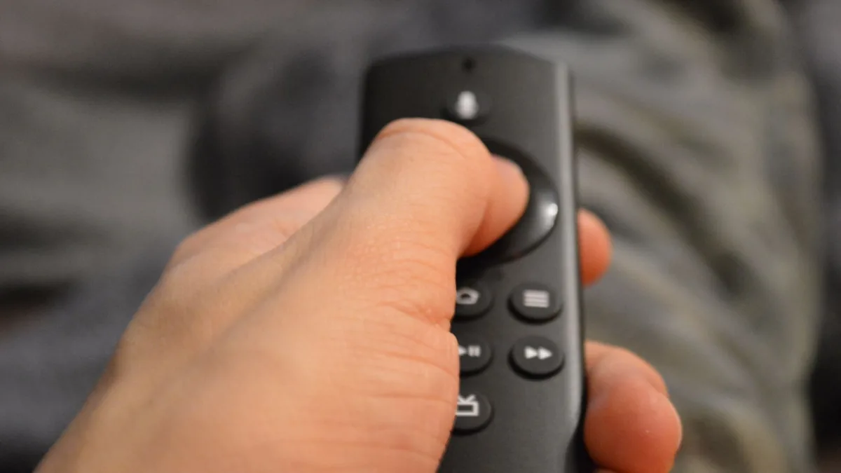 Telecomanda noului Fire TV Stick 4K pe o masă, lângă un televizor